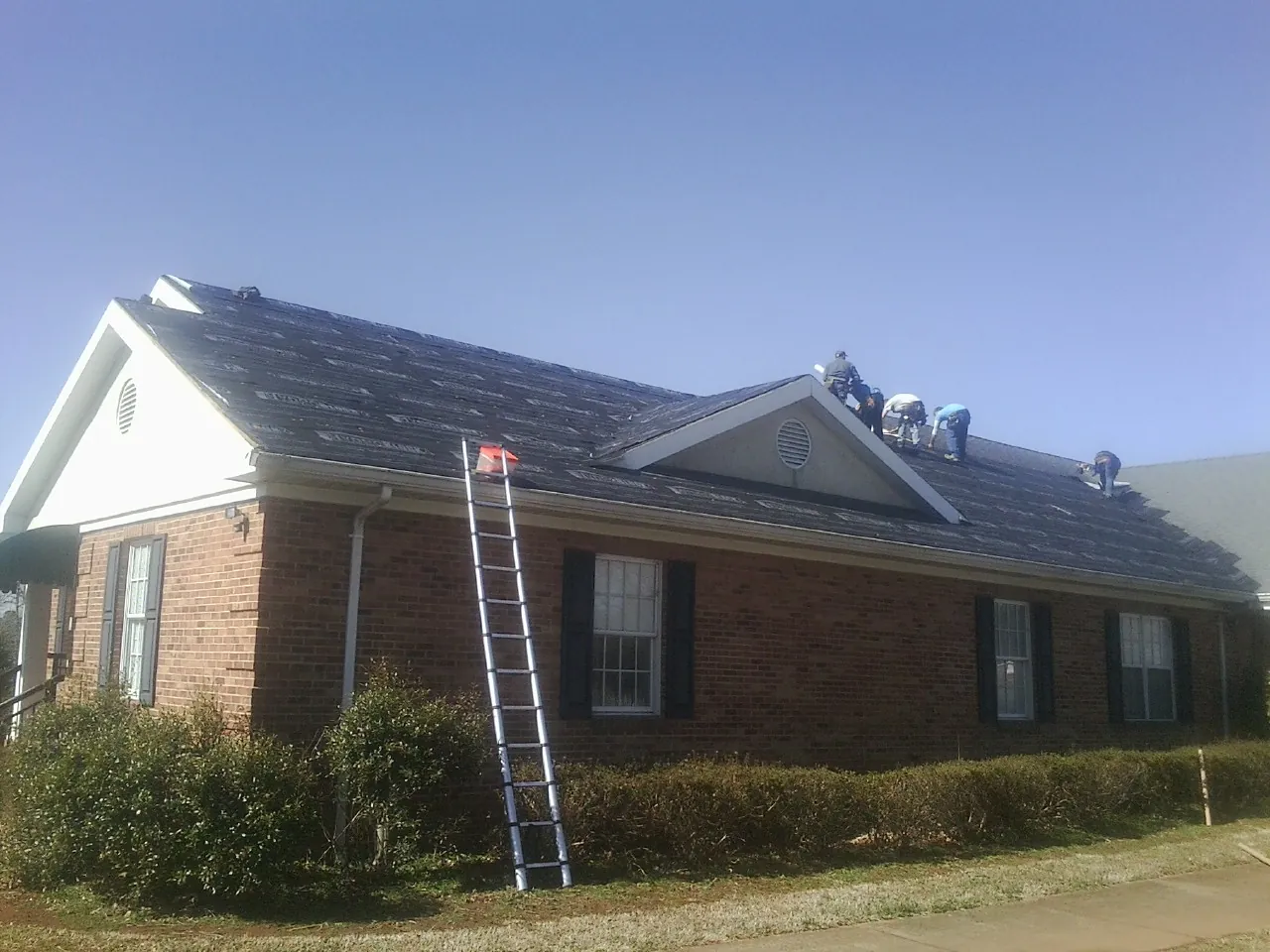 Crew tearing shingles off a brick ranch roof with a ladder set — Emergency Roof Repair work by our crew in West Harrison